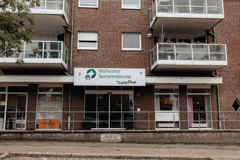 Straßenansicht des Eingangs zur Tagespflege Saarn unter Balkonen eines Backsteingebäudes.