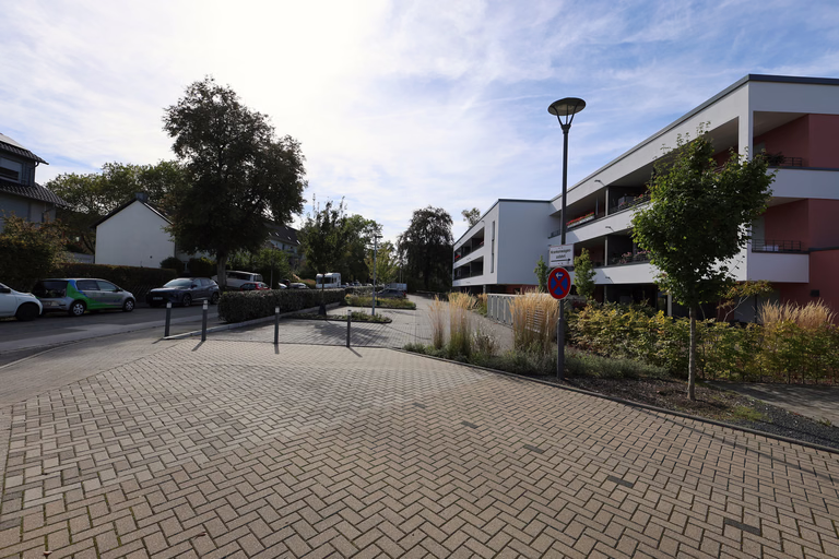Helles Wohngebäude mit Balkonen und gepflastertem Vorplatz.