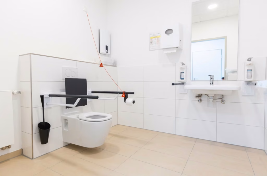 Sanitärraum mit Toilette, klappbaren Haltegriffen, Waschbecken und Notrufzug.